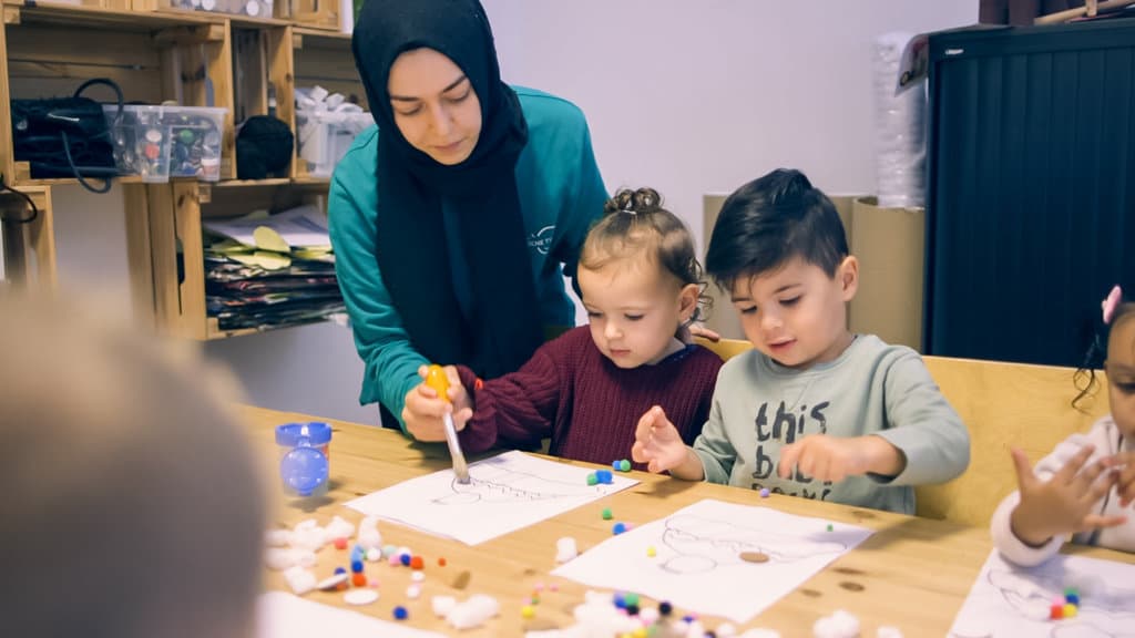 Pedagogisch professional knutselt met peuters aan tafel